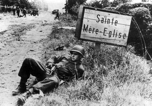 A US trooper poses by the Sainte Mere-Eglise road sign