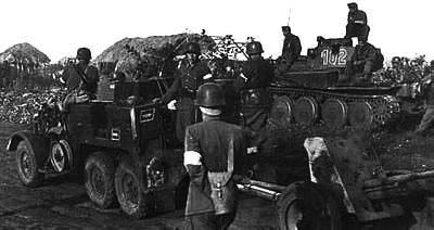 Anti-tank gunners pass by a halted T-38G tank