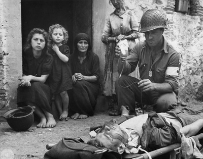 A US Medic attends a wounded soldier as some Sicilians look on